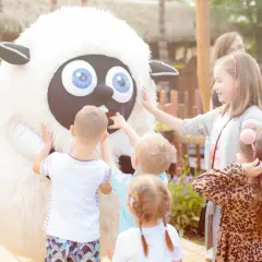 Dzieci bawią się z pluszową owcą, szukając pomysłu, gdzie na weekend z dzieckiem jesienią. Radość i zabawa na świeżym powietrzu.