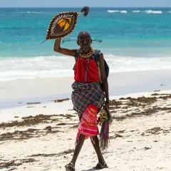 Kenia, lipiec: mężczyzna w tradycyjnym stroju z tarczą na plaży, piękna pogoda i turkusowe morze.
