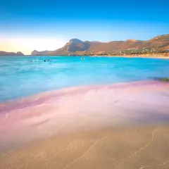 Piękna plaża w Grecji, gdzie pogoda w lutym pozwala na kąpiel w turkusowym morzu. W tle góry i kurort.