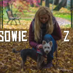 Jesień w Górach Sowich z psem. Kobieta w bordowej kurtce klęczy wśród opadłych liści, głaszcząc swojego małego, kudłatego pupila.