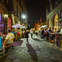 Wieczór na ul. Piotrkowskiej w Łodzi. Ludzie siedzą przy stolikach w restauracjach, ciesząc się atmosferą.