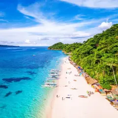 Rajska plaża na Filipinach, gdzie turkusowa woda spotyka biały piasek. Nawet podczas pory deszczowej, słońce przebija się przez chmury, a łodzie czekają na turystów.