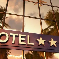 Hotel z czterema gwiazdkami, odbijający palmy i samolot w zachodzącym słońcu.
