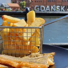 Ryba z frytkami na talerzu, w tle napis GDAŃSK. Idealne miejsce, gdzie zjeść w Gdańsku.