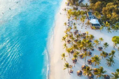 Rajska plaża na Zanzibarze w grudniu. Turkusowa woda, biały piasek, palmy i leżaki. Idealna pogoda na wakacje.