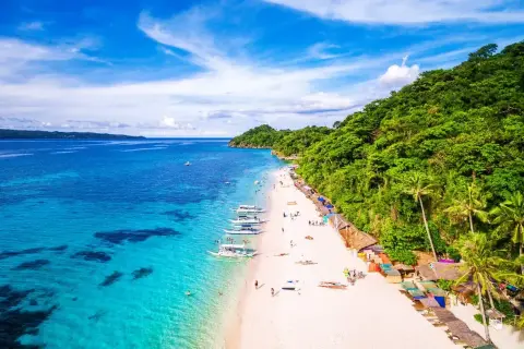 Rajska plaża na Filipinach, gdzie turkusowa woda spotyka biały piasek. Nawet podczas pory deszczowej, słońce przebija się przez chmury, a łodzie czekają na turystów.