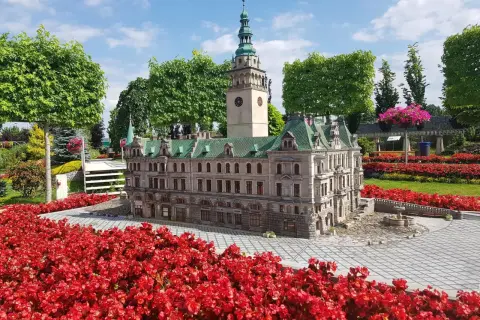 Miniaturowy ratusz z wieżą i zegarem, otoczony czerwonymi kwiatami. Idealne atrakcje dla dzieci Kotlina Kłodzka.